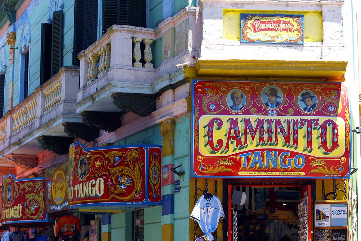 A festive tango scene in Buenos Aires, with red and yellow signs on the shops and entryways.
