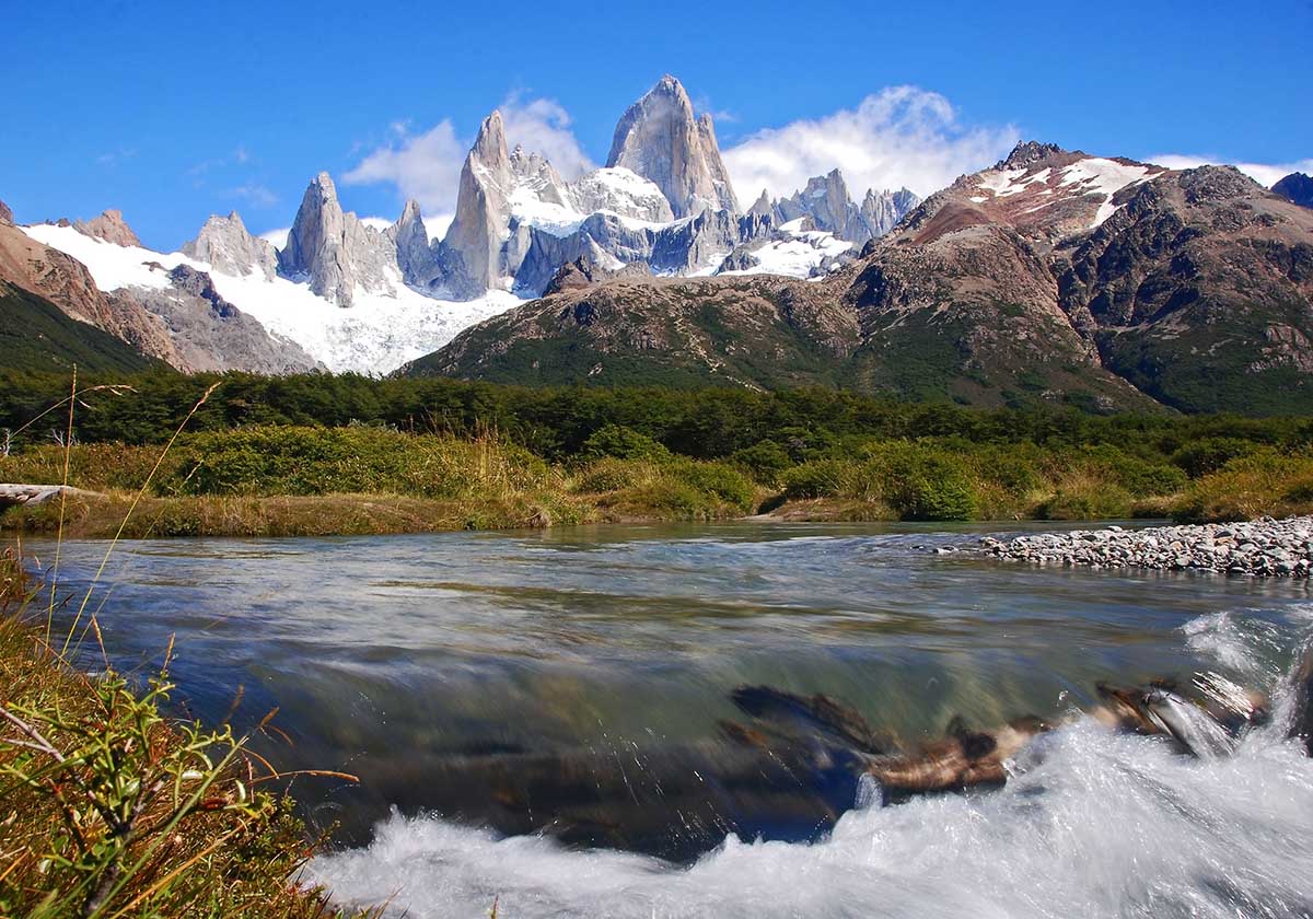 Rushing river with treed coasts and soaring peaks of El Chalten in Argentina's Patagonia region.