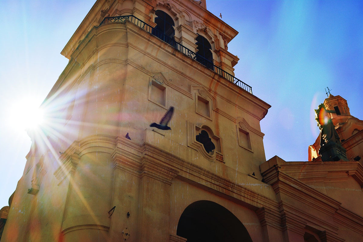 The sun shining on a colonial church in Córdoba, Argentina as a pigeon flies past.