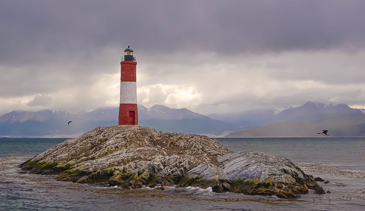 A lighthouse on a rock formation in the Beagle Channel, with mountains visible in the distance.