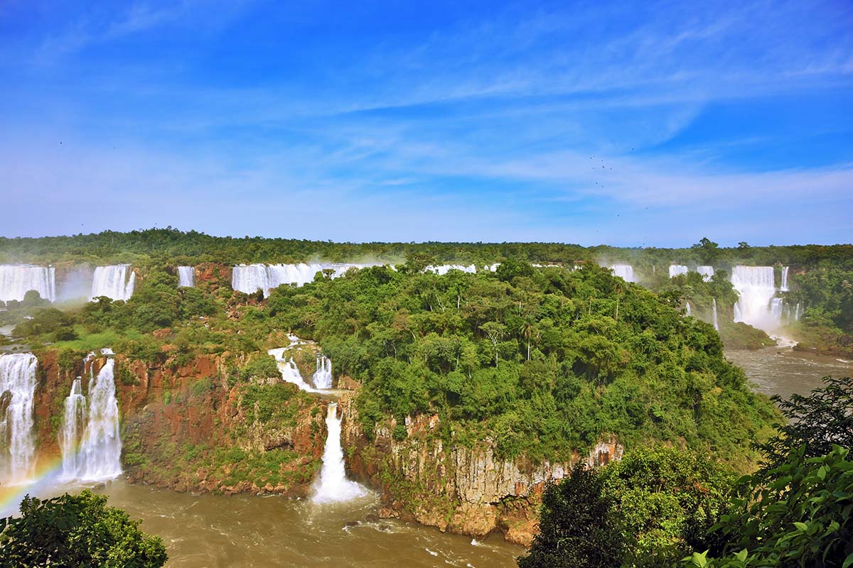 A rainbow forming amidst the numerous waterfalls and jungle landscapes of Iguazu Falls.