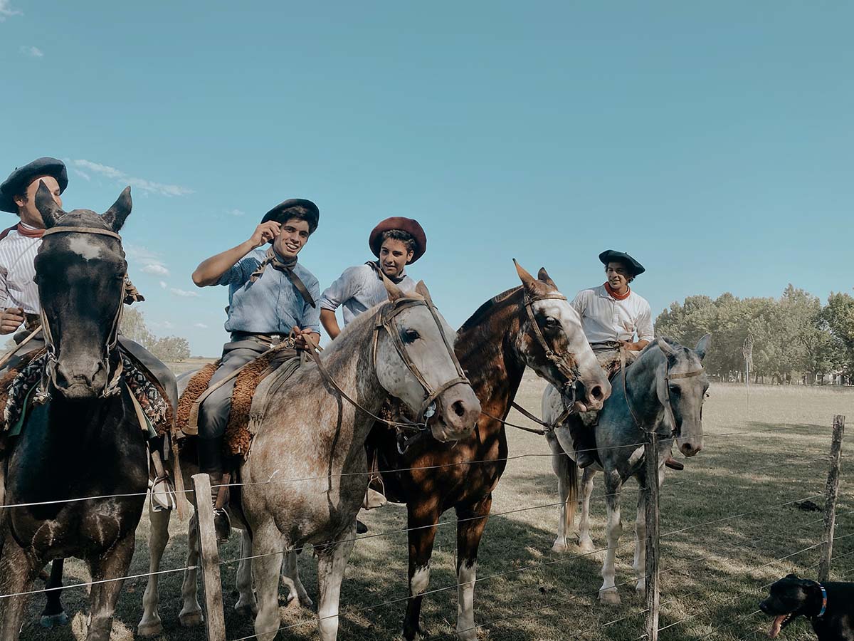 Four men in traditional gaucho attire ride horses across a field in San Antonio de Areco.