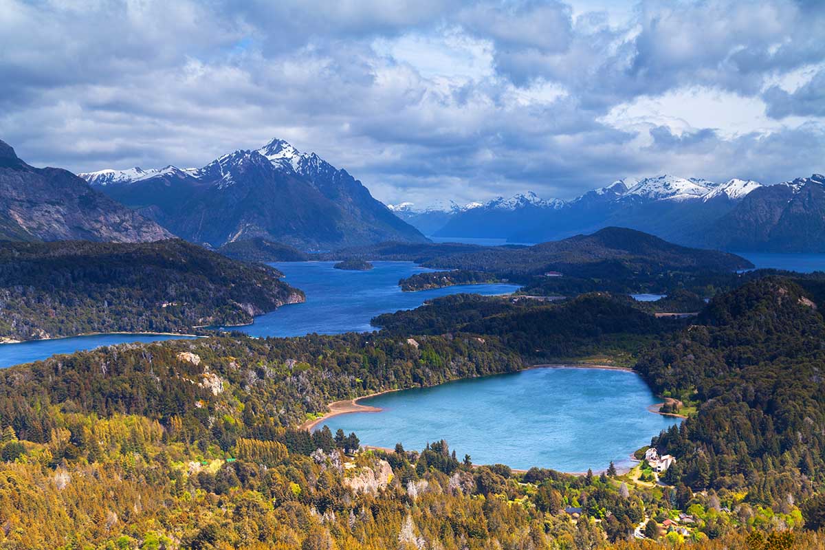 The stunning glacial lakes and snow-capped mountains of Bariloche on a partly cloudy day.