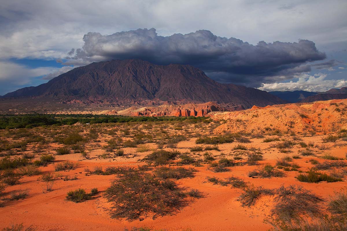Red sand desert and red-colored mountains under a cloudy sky in Salta, Argentina.