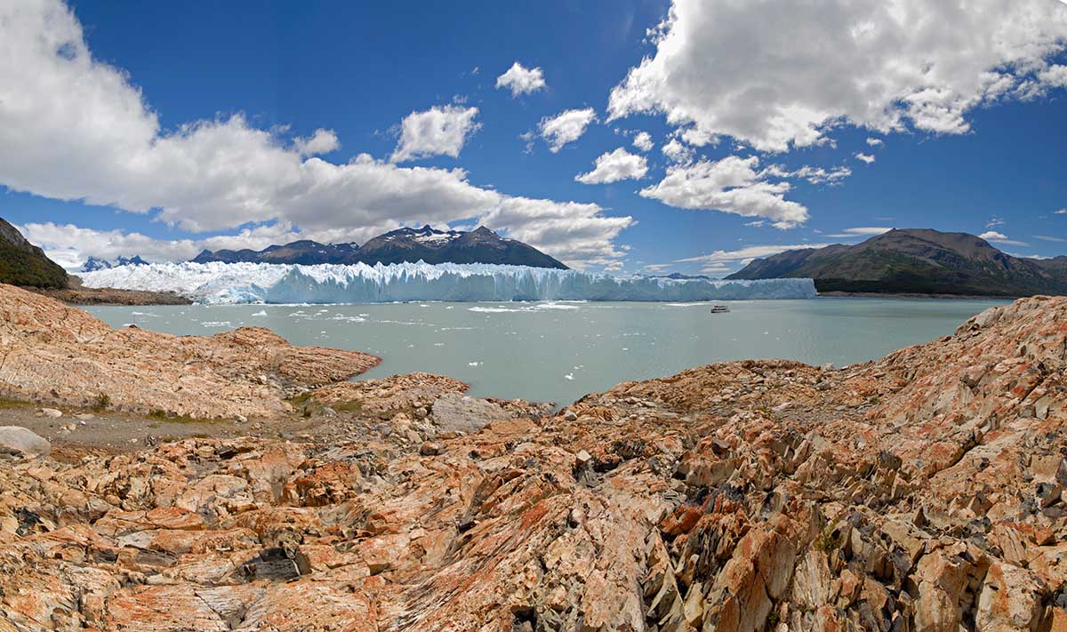 Rocky coast, glaciers, mountains and blue partly cloudy skies at Parque Nacional Los Glaciares.
