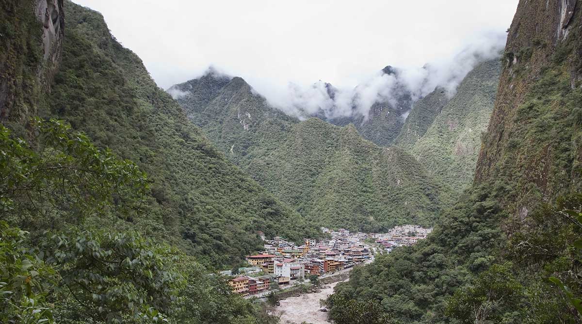 Small colorful cluster of buildings in Aguas Calientes surrounded by towering green mountains. 