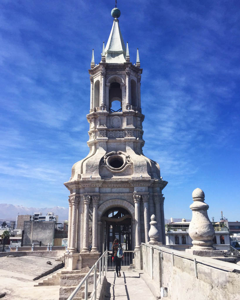 Woman with backpack walks towards the steeple of the Arequipa Cathedral rooftop