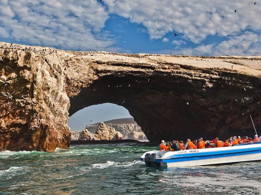 A boat passes by an arch rock formation jutting out of the water on a Ballestas Islands tour.