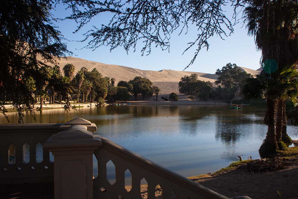 View of Huacachina Oasis in Peru, a lush green lagoon surrounded by tall sand dunes