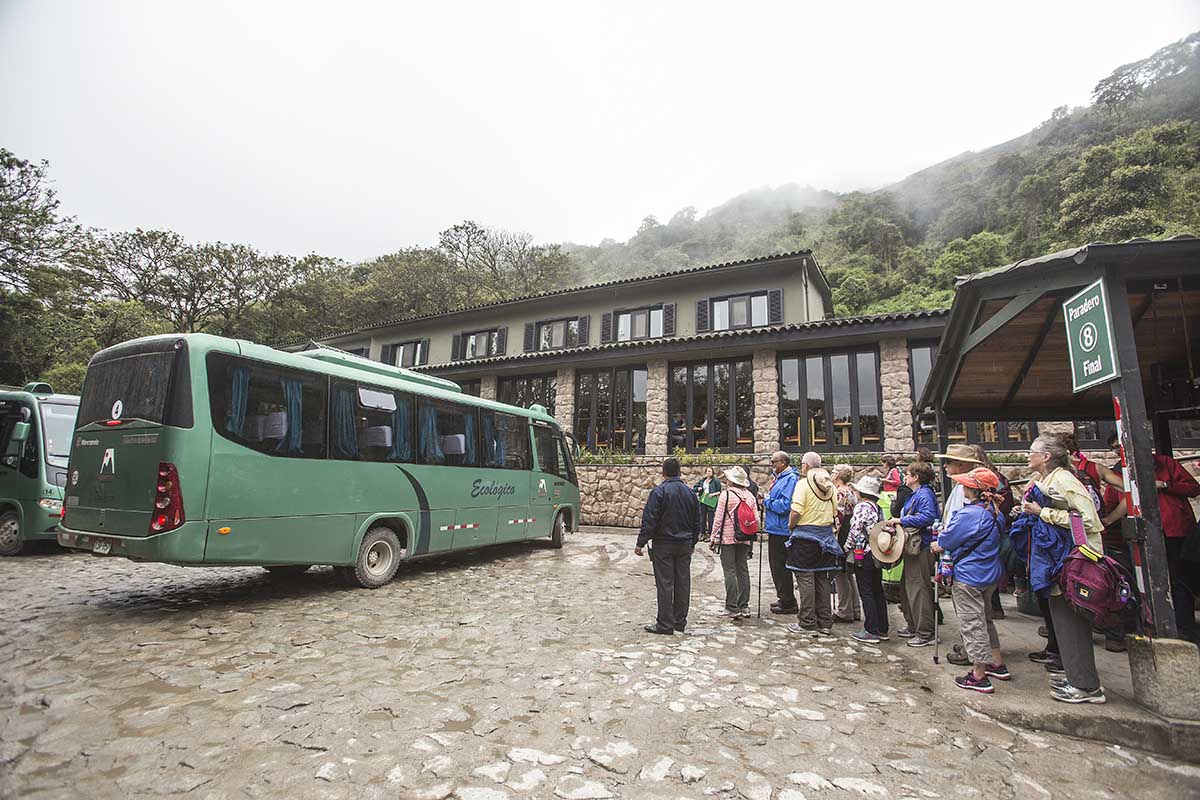 A crowd of Machu Picchu visitors waiting to board the green shuttle bus to Aguas Calientes.