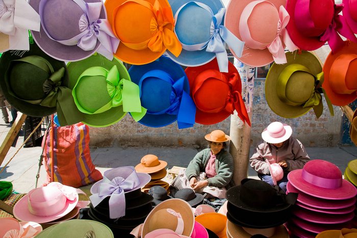 A couple of women selling an assortment of different colored hats at a Peruvian market.