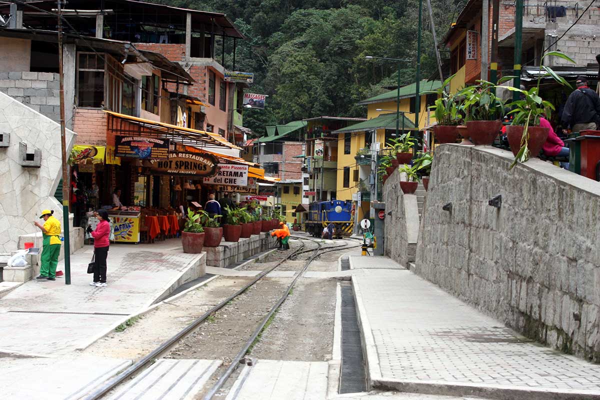 A street in Aguas Calientes, Peru with train tracks down its center and lined by restaurants.