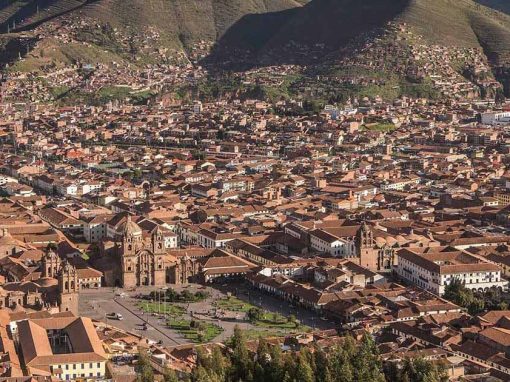 Looking down on Cusco plaza and surrounding areas. Brown tiled rooftops and mountains behind.