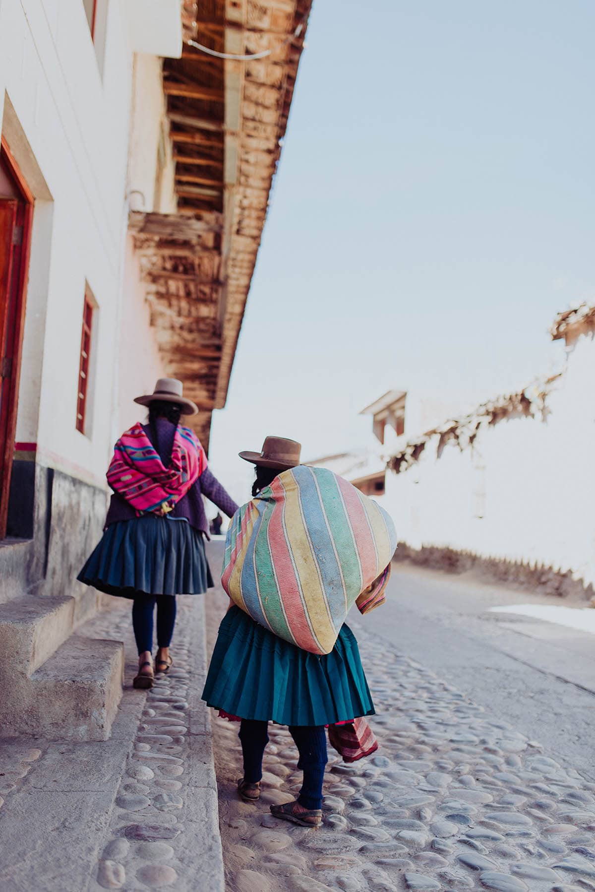 Andean women walk down a cobblestone street in Peru