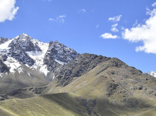 Landscape of snow-covered mountains and yellow-green hills in the Peruvian Andes Mountains.