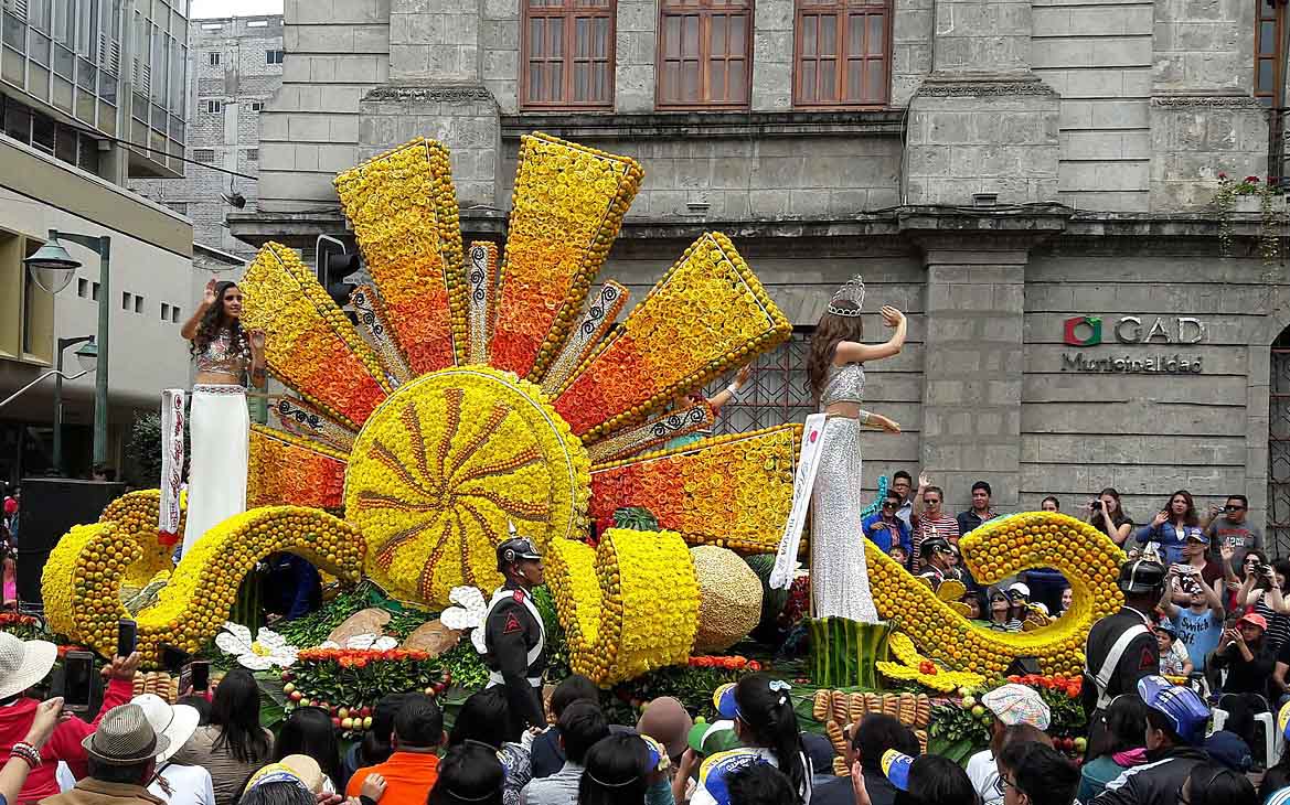 A floral float in a Carnival parade with two women waving to the crowds.