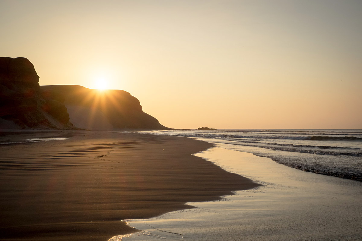 Sunset behind cliffs framing the smooth sandy beach of Chicama.