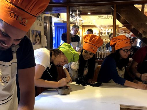 Group of 4 young adults with apron and chefs hat grinding cacao beans at a chocolate-making workshop
