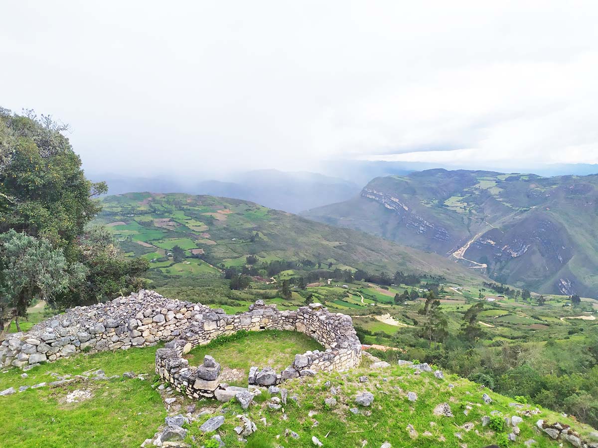 Kuelap covered in clouds with mountain views in the distance.