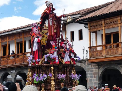 A procession makes its way past some historic buildings with balconies at Corpus Christi in Cusco.