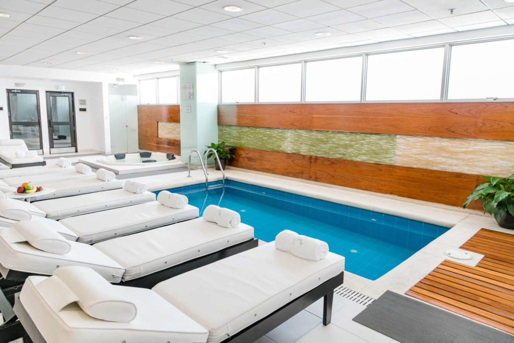 A pool and hot tub with several white lounge chairs.