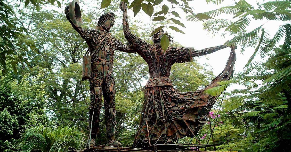 Two human statues made of metal pieces dancing cumbia together with greenery surrounding them.