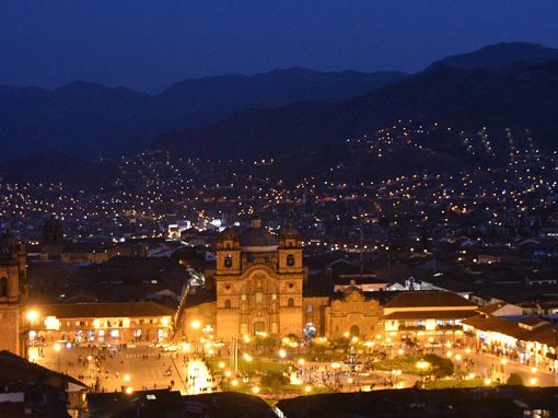 A brightly-lit view of Cusco city's main Plaza de Armas at night.