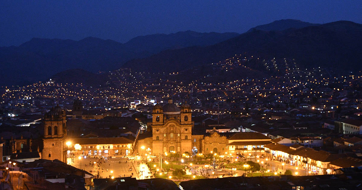 A brightly-lit view of Cusco city's main Plaza de Armas at night.