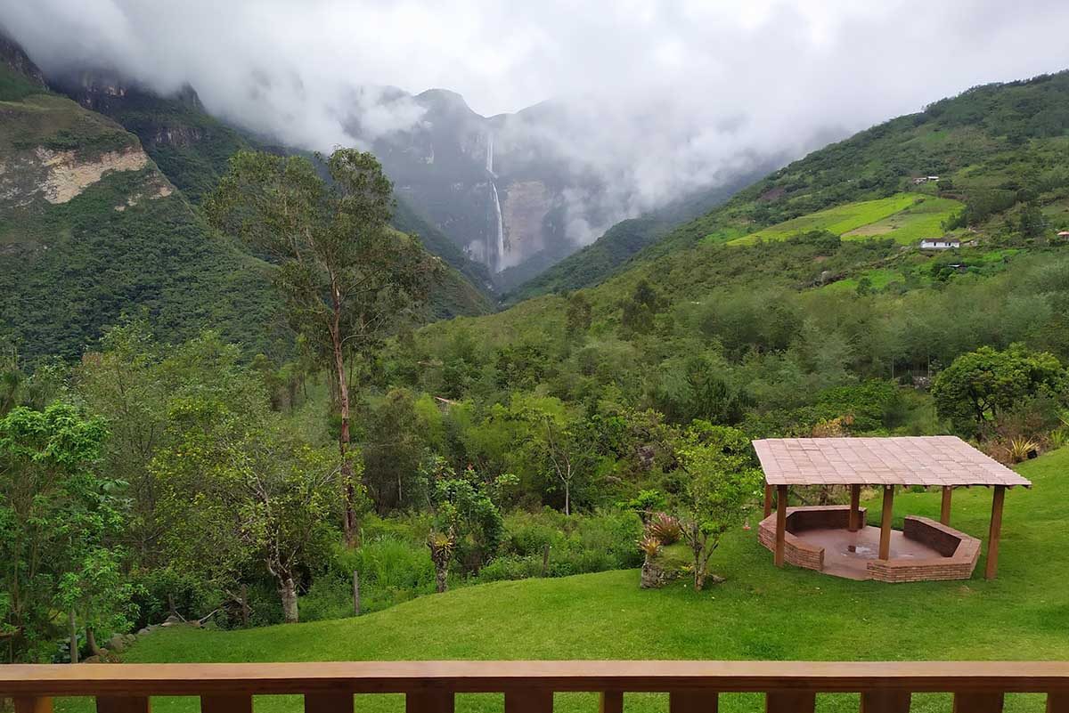 Lush green, mountainous landscape leading to a waterfall under clouds in the distance.