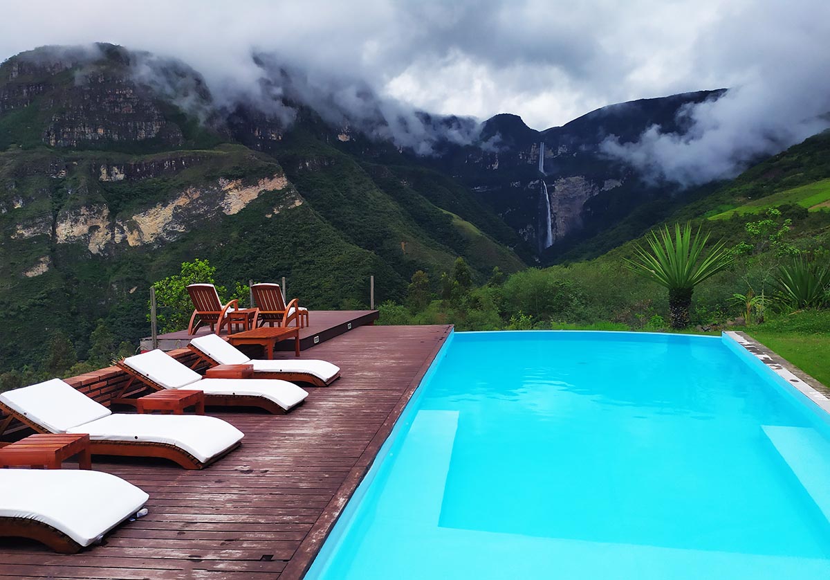 A long blue pool with lounge chairs to the side looks over the Gocta Waterfall in the distance.