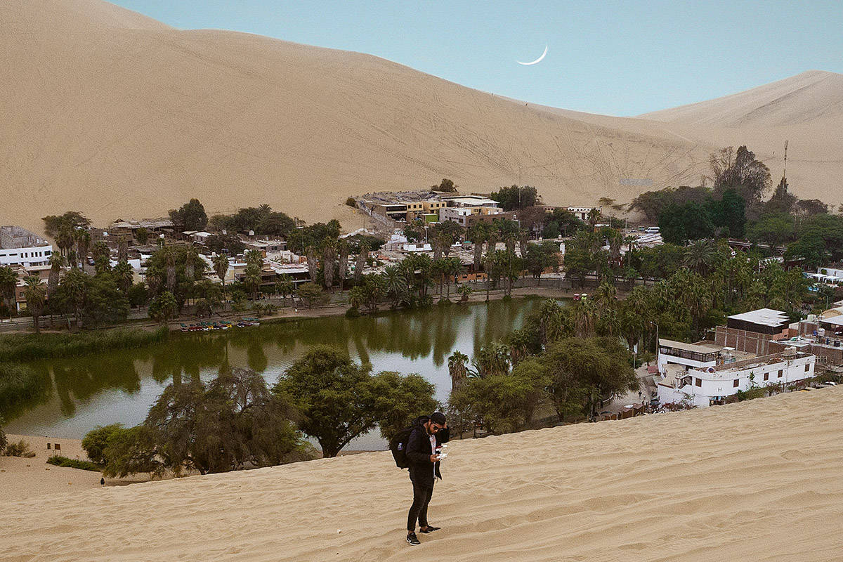 A man walking in the sand in front of the Huacachina Oasis