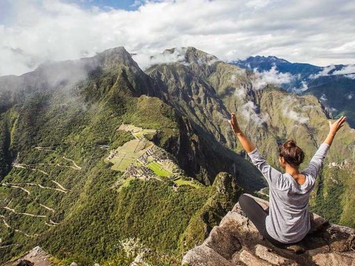 A visitor at the Huayna Picchu viewpoint with arms outstretched, looking at the ruins below.