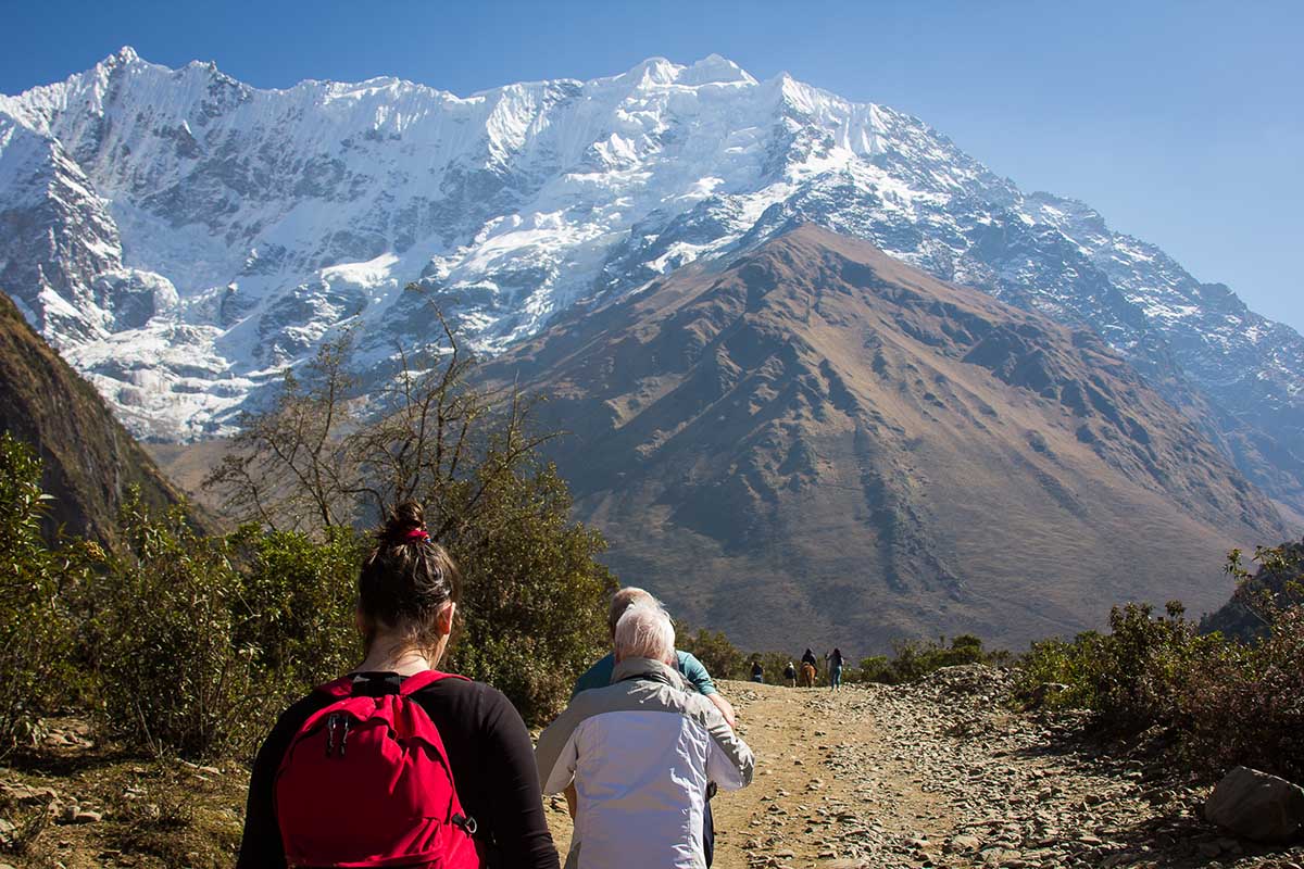 Three hikers on the flat part of the Humantay trail with snow-capped mountains in the distance.