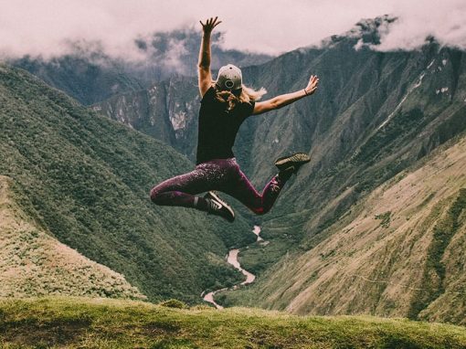 A female tourist jumping into the air at Machu Picchu with the Urubamba River as a backdrop.