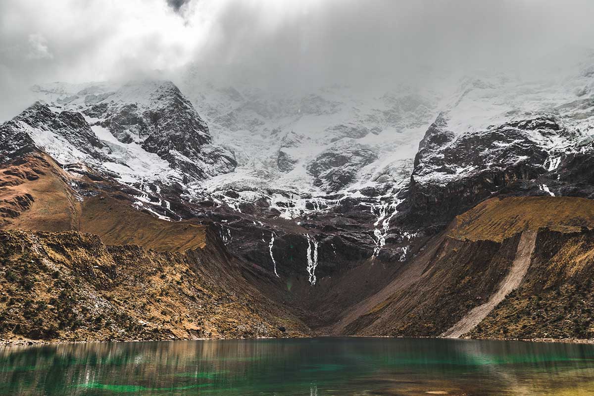 Clouds hang over the mountain glaciers of Humantay while the green lake is still visible below.