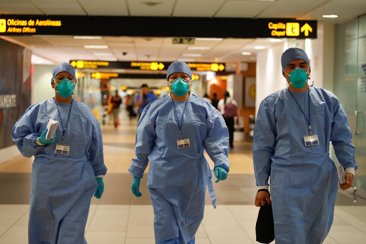 Three doctors walking in the Lima airport using blue medical caps, masks, gloves, and clothing.