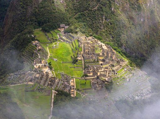 The hilltop Inca city of Machu Picchu surrounded by green mountains and white cloudy mist.