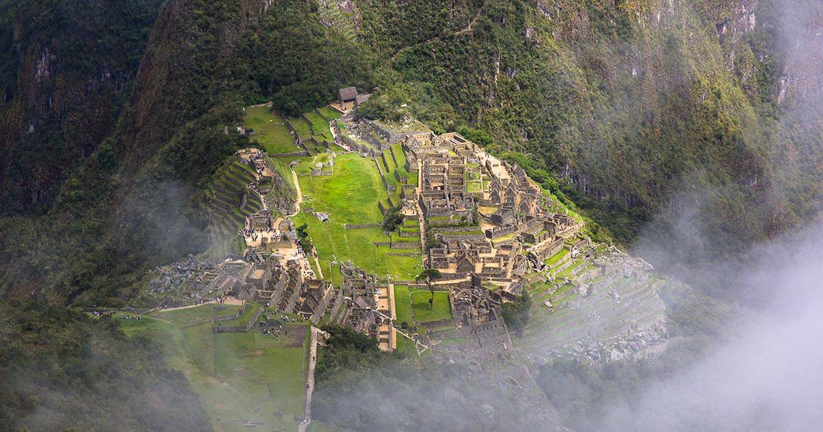 The hilltop Inca city of Machu Picchu surrounded by green mountains and white cloudy mist.