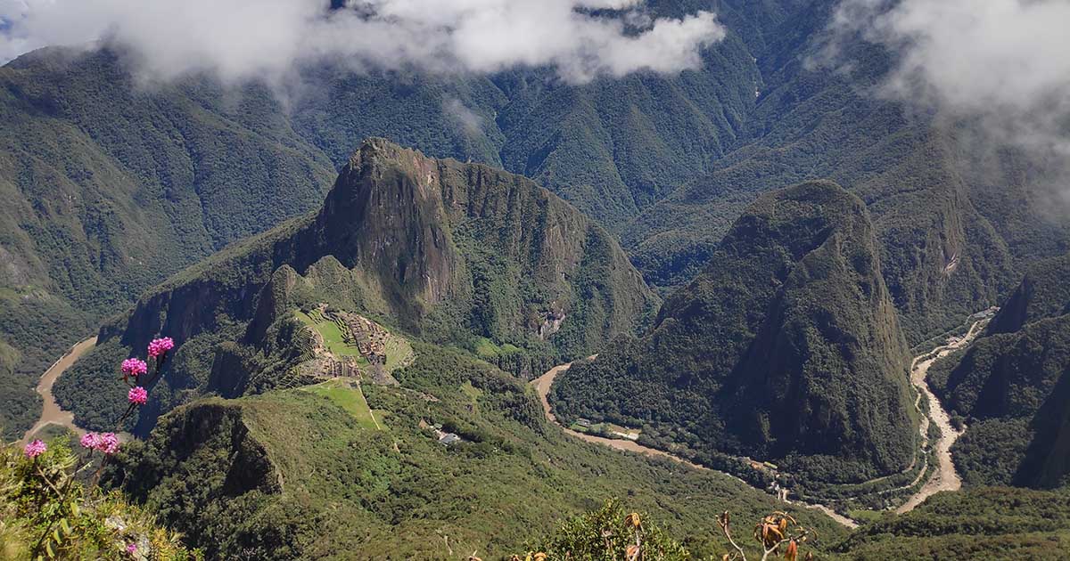 Aerial view of Machu Picchu stone ruins surrounded by green mountains and clouds.