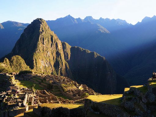 Machu Picchu ruins bathed in sunlight as a group of tourists overlook the ruins.