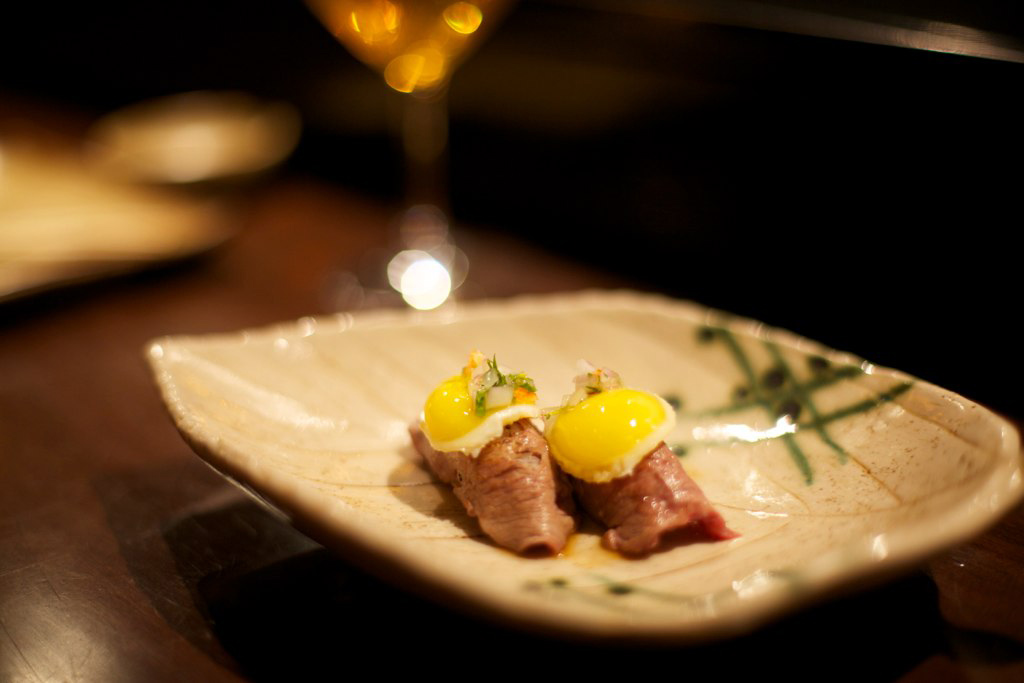 A dish from Maido. Two pieces of cooked red meat garnished with yellow egg yolks on a ceramic plate. 