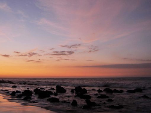 Sunset over the Pacific ocean dotted with lava rocks from Mancora beach in Northern Peru.