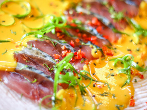 Colorful nikkei food including raw fish in a bright yellow sauce with red peppers and green garnishes.