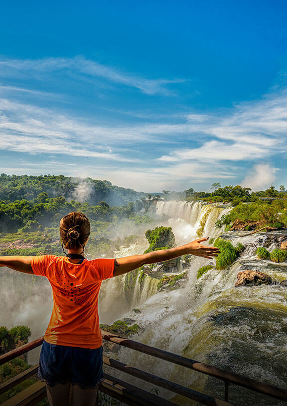 A person stretches their arms to the side while overlooking massive waterfalls at Iguazu Falls