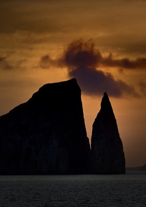 A sunset silhouettes Kicker Rock, a jagged rock formation jutting out of the ocean in the Galapagos