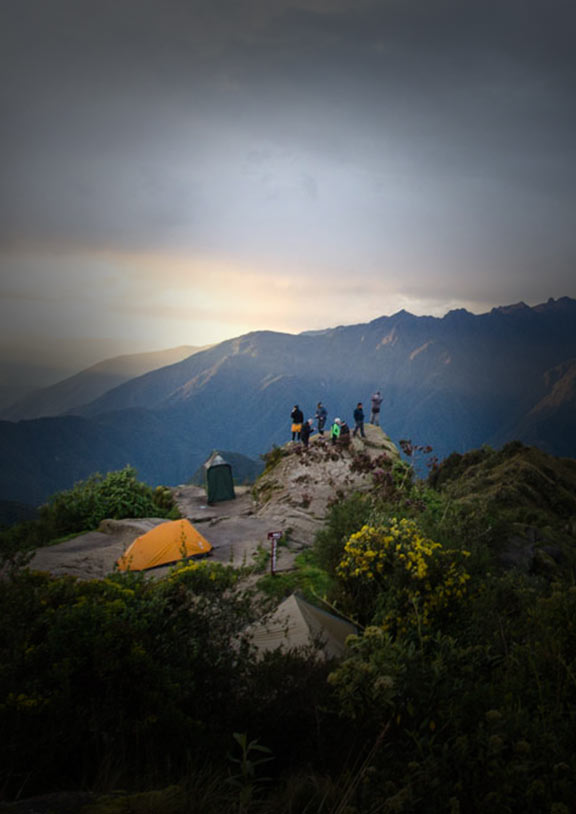 Inca Trail campsite with tents set up and trekkers on a ledge peaking over mountainous terrain