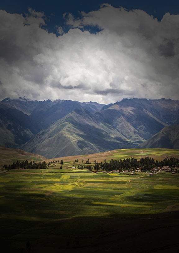Vast green landscape in the Sacred Valley with Andes Mountains behind and clouds above