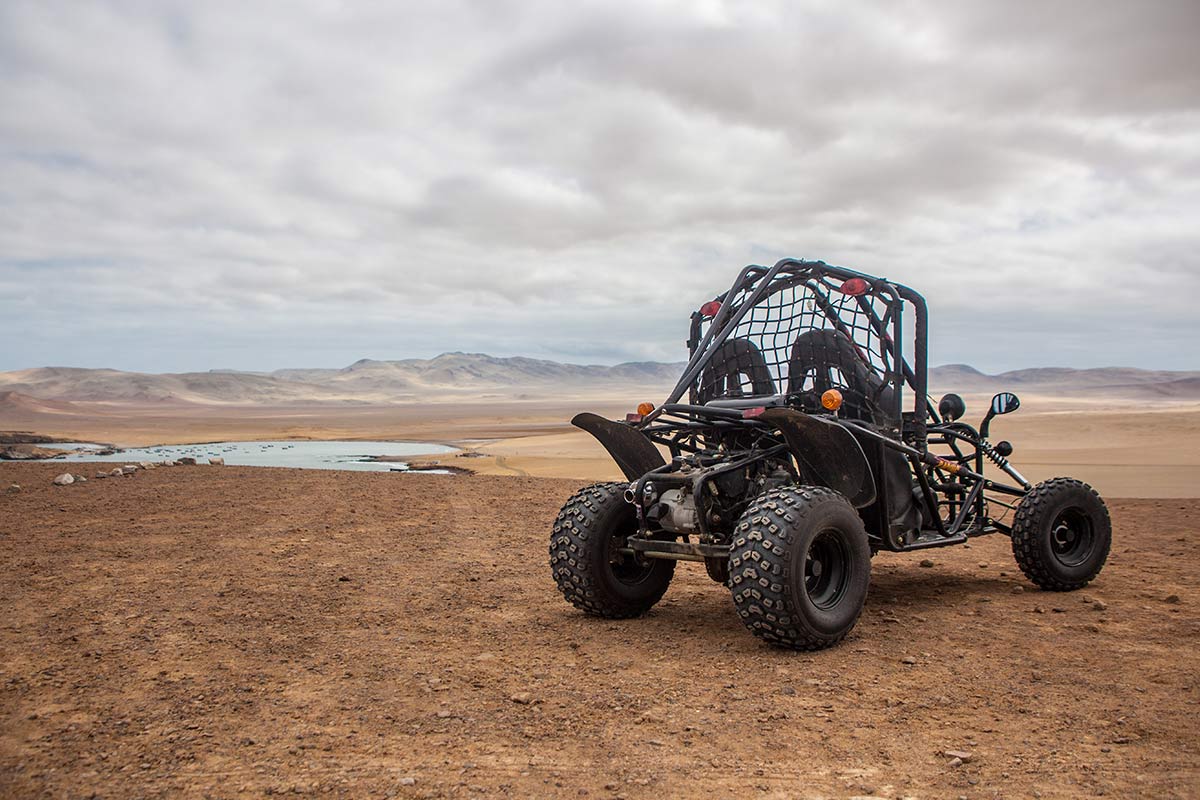An open air quad bike parked on a hill overlooking the Paracas Peninsula on a cloudy day. 