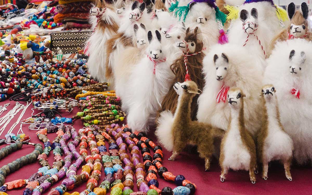 Fluffy llama dolls next to colorful bracelets and necklaces at a Peruvian souvenir market.