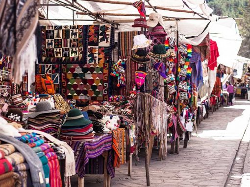An outdoor Peruvian market. Stalls are selling alpaca scarves, hats, pompoms, and wall hangings.